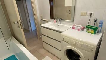 Un bagno con vasca, lavatrice, lavandino e specchio.