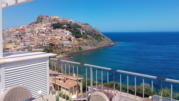 Un balcón con vista a un pueblo costero, que incluye una colina con edificios y una fortaleza.
