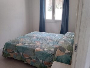 Een slaapkamer met een bed, een raam met gordijnen en een deur.