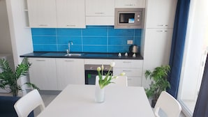 Una cocina moderna con armarios blancos, un salpicadero azul y un microondas. Hay una mesa de comedor con sillas y un florero con flores.