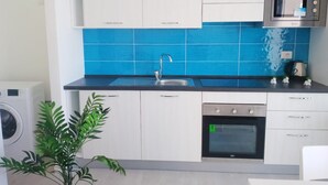 Una cocina moderna con armarios blancos, salpicadero azul, microondas de acero inoxidable y horno empotrado.