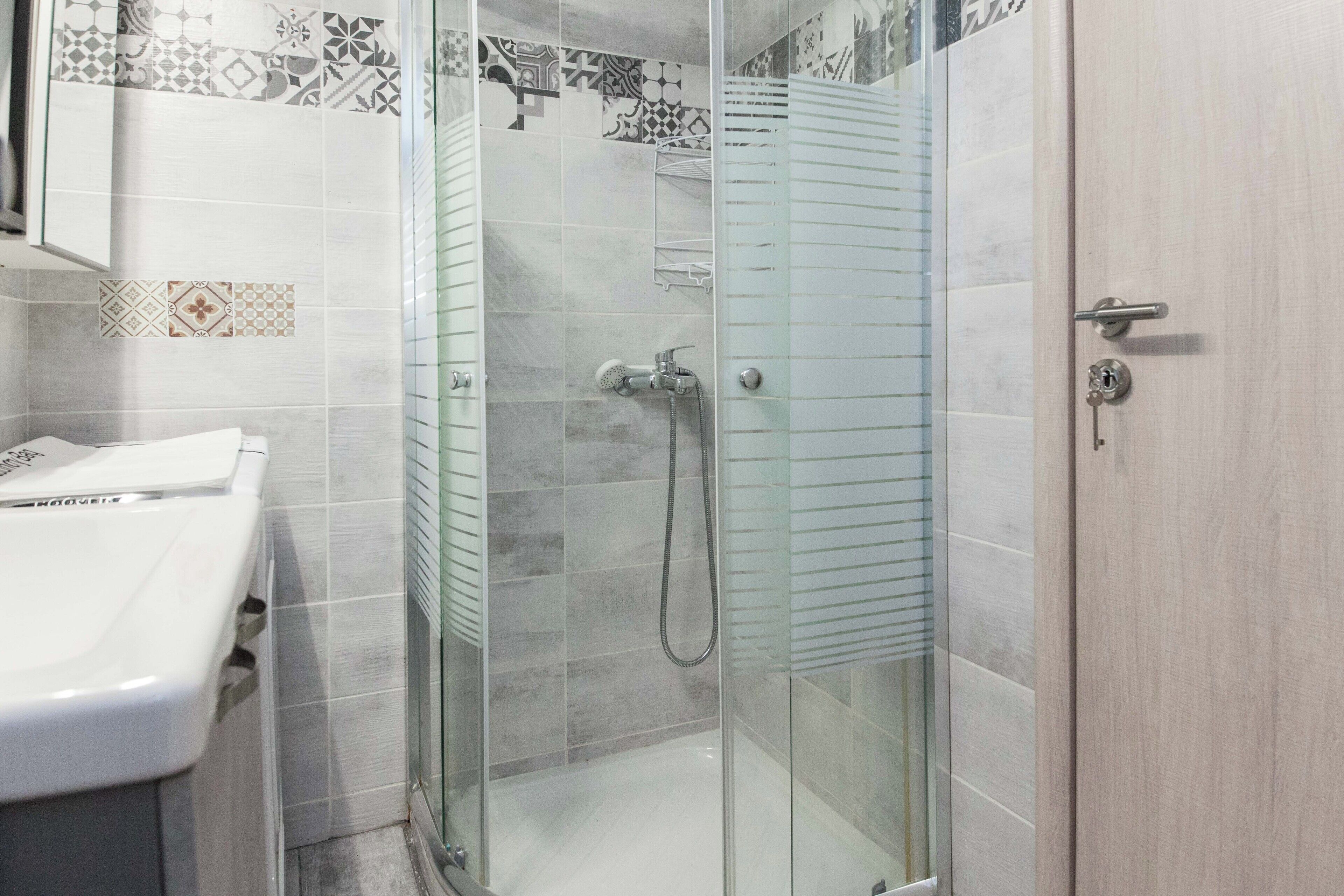 Un bagno moderno con doccia vetro, lavandino bianco e piastrelle decorate sulle pareti.