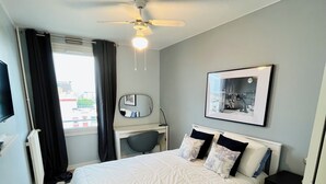 A hotel room with a bed, a ceiling fan, a mounted TV, a bedside table, a chair, a window with curtains, and a framed picture on the wall. - Entire rental unit in Maisons-Alfort, France (Maisons-Alfort)