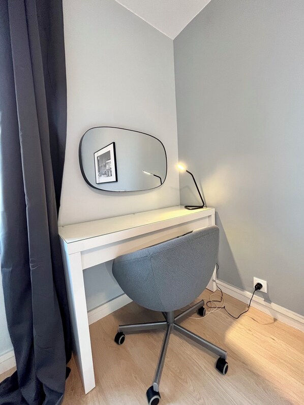 Un bureau moderne avec une chaise grise, un miroir fixé au mur et une lampe de bureau.