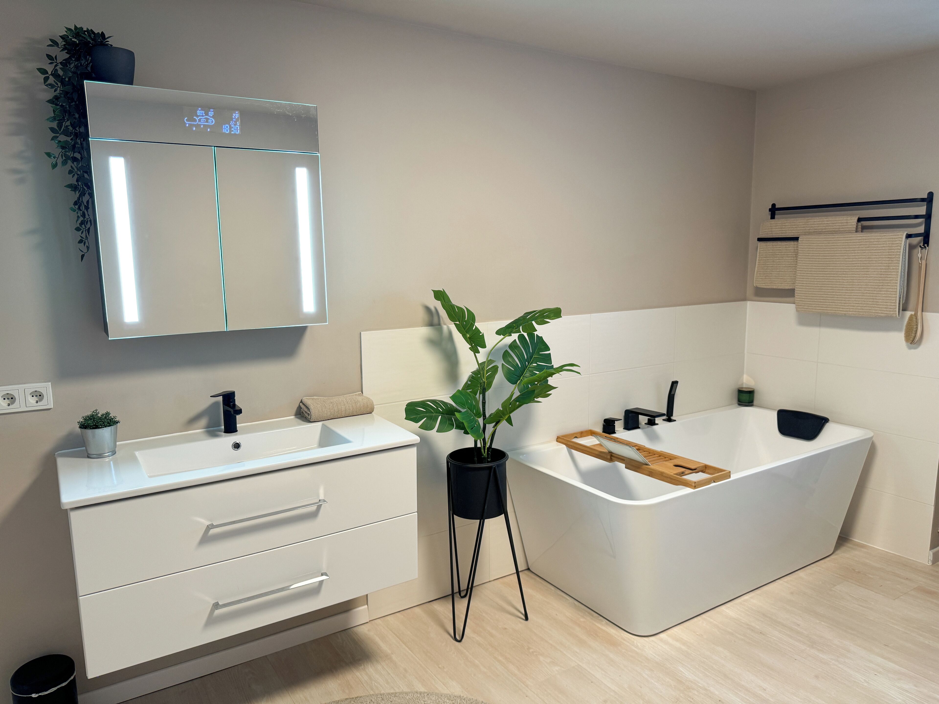 A modern bathroom with a white sink, mirror, and bathtub. There is a plant on the floor and a towel on the counter.