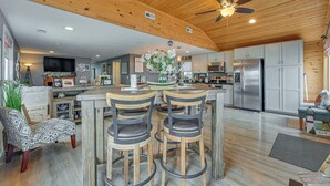 A spacious kitchen with wooden ceiling beams, a central island with bar stools, and modern appliances. - Angler's Cottage on Lake Cornelia: Pets Welcome! (Clarion)
