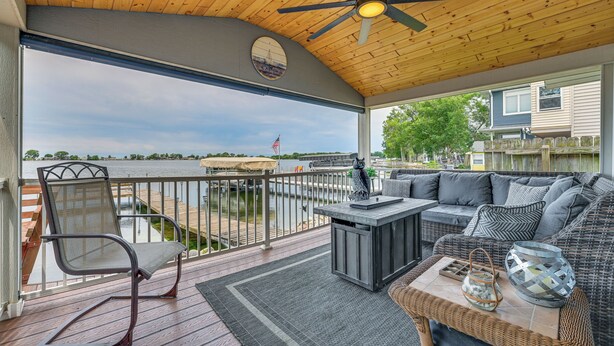 A covered outdoor deck with a wooden ceiling, a round window, a sofa, a table, and a chair. - Angler's Cottage on Lake Cornelia: Pets Welcome! (Clarion)