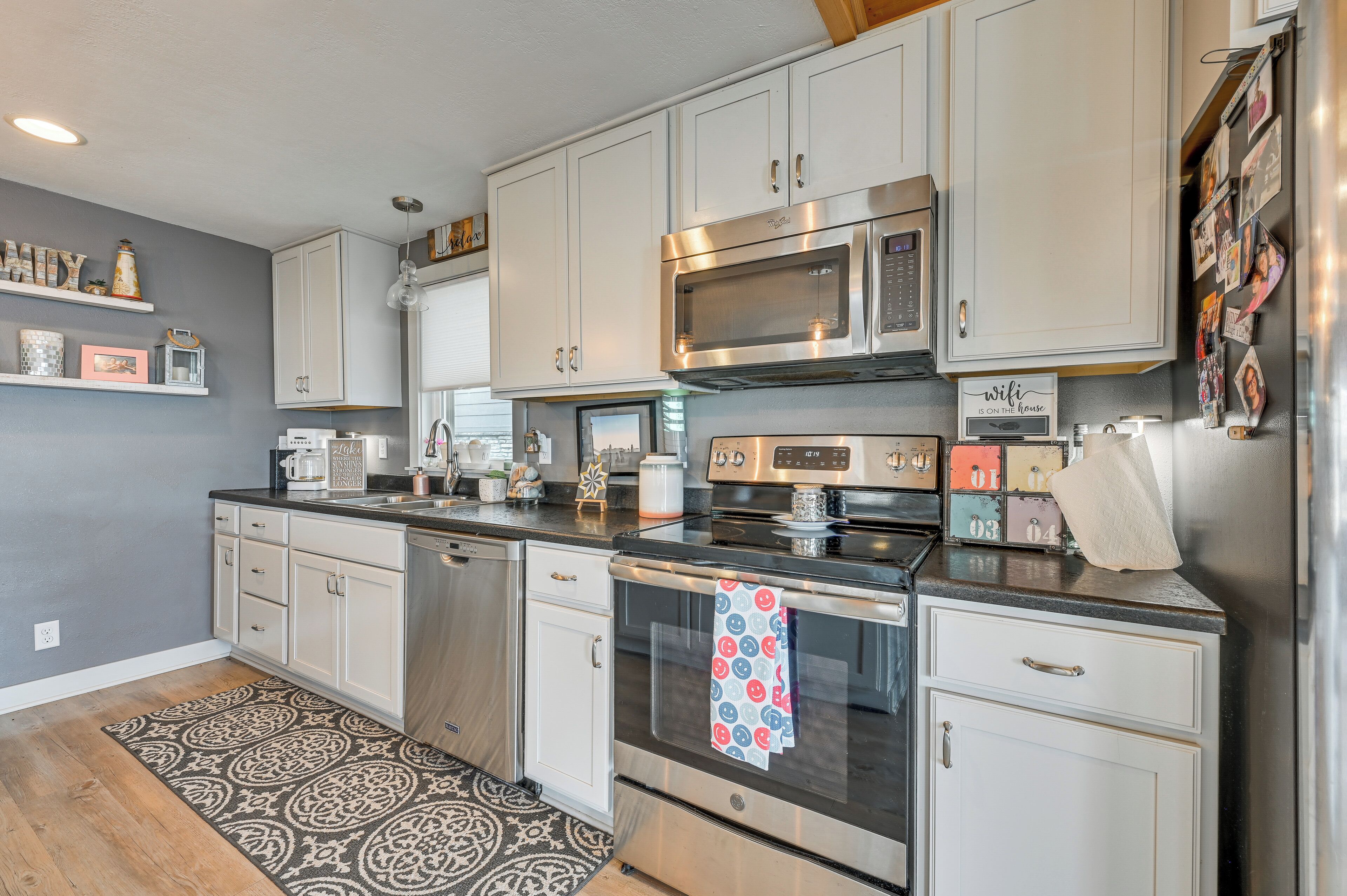 A modern kitchen with stainless steel appliances, white cabinetry, and decorative items on shelves.
