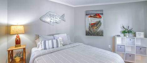 Un dormitorio con cama, un adorno de pez montado en la pared, un cuadro de un barco, una lámpara y un mueble de almacenamiento.