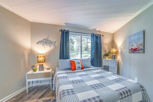 Un dormitorio con una cama grande, una mesita de noche con lámpara, una ventana con cortinas y una decoración de peces colgada en la pared.