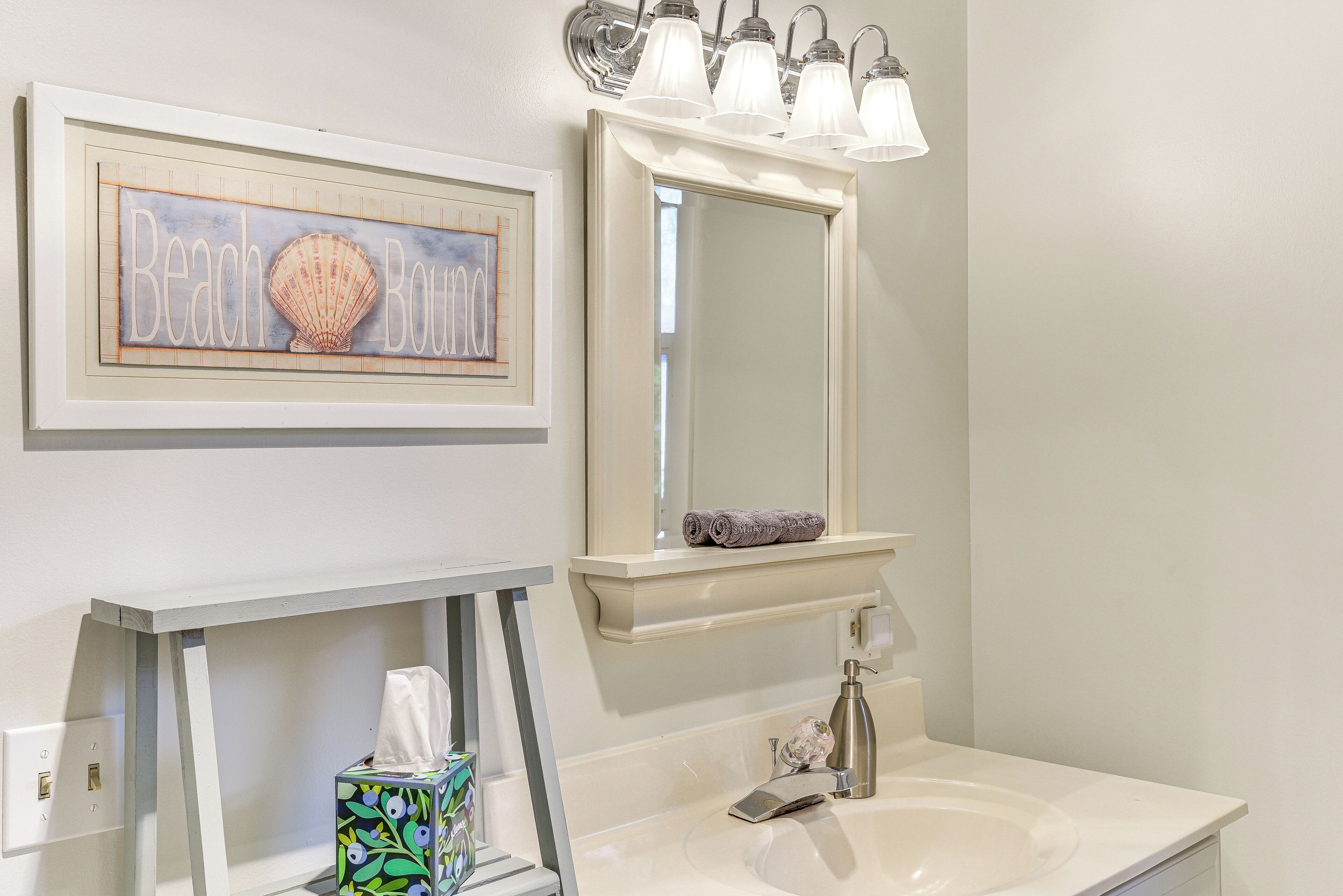 A bathroom with a white sink, a mirror above it, and a framed artwork with a seashell design.