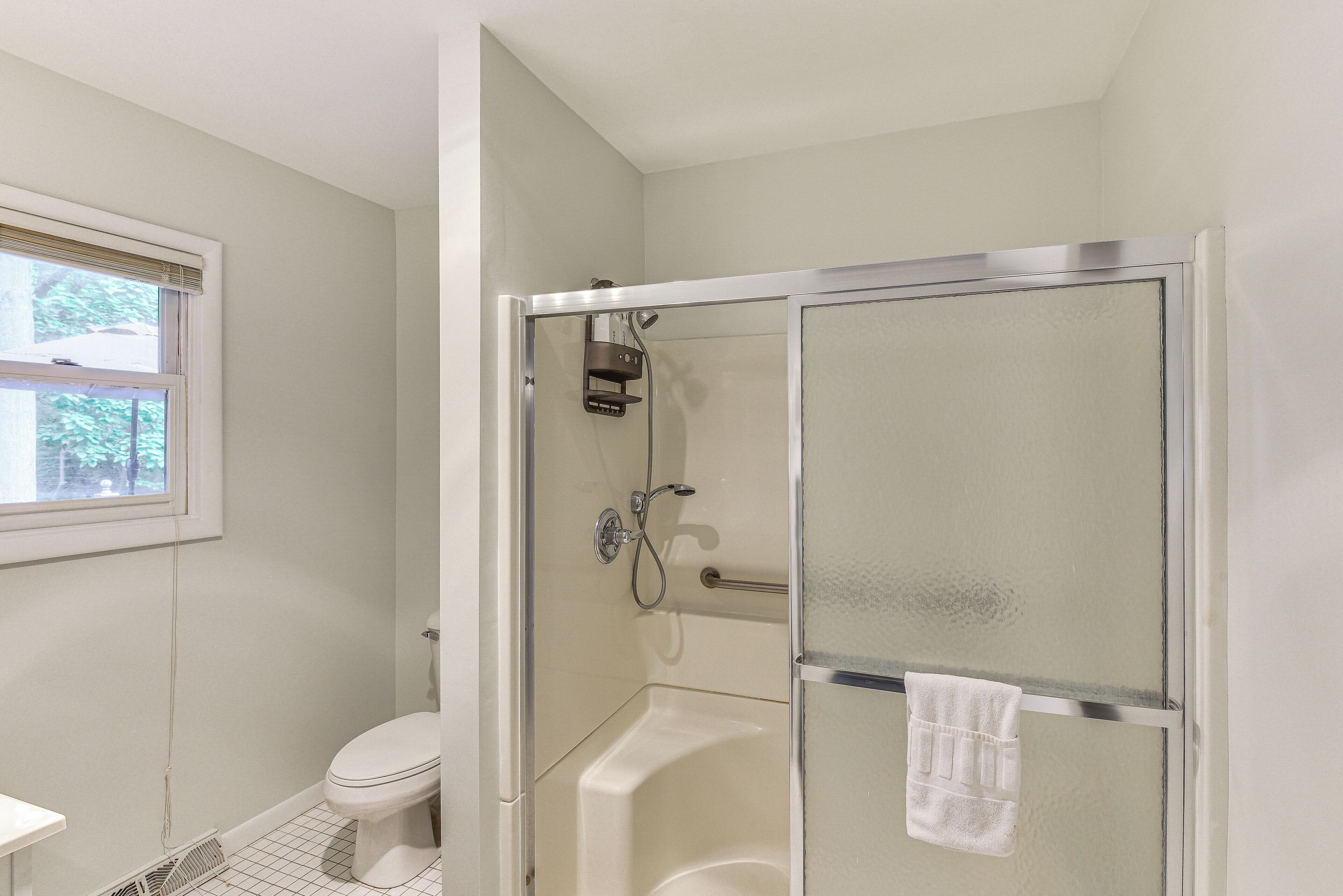Ein Badezimmer mit Toilette, einer Dusche mit Glastür und einem Fenster mit Jalousien.