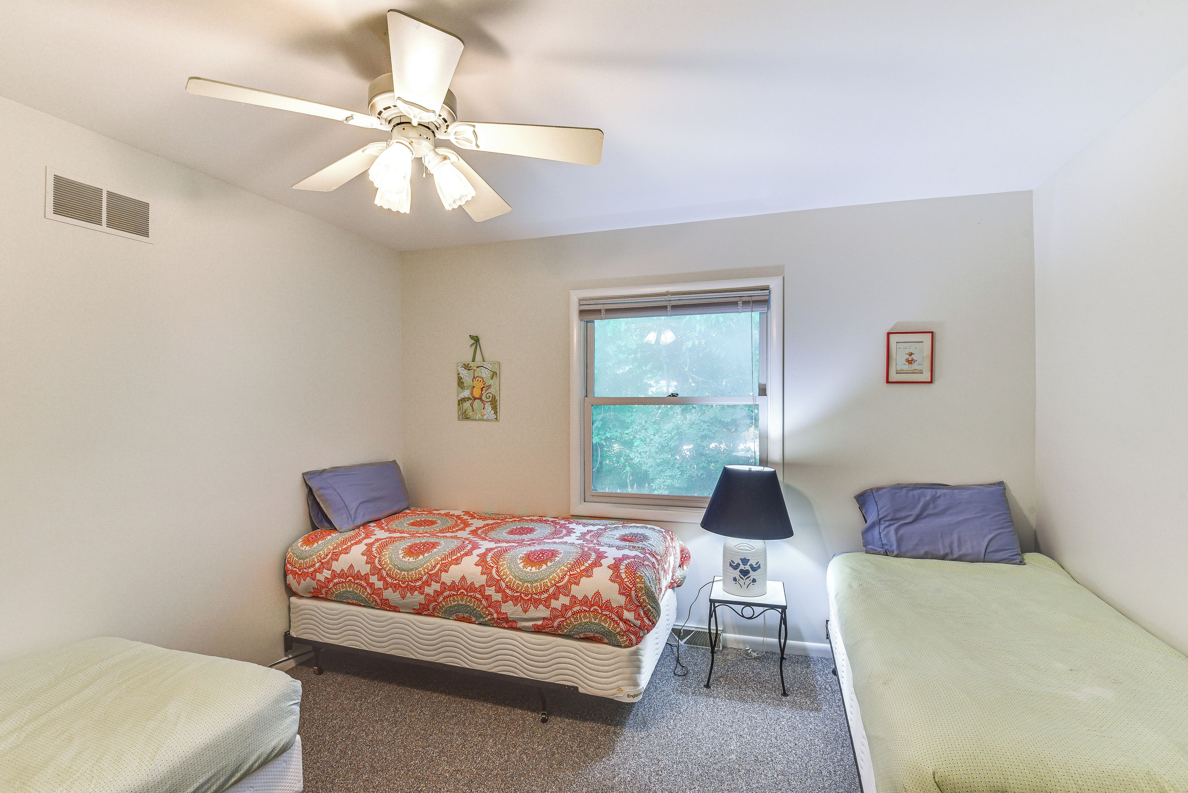 A bedroom with a bed, two bedside tables, a ceiling fan, a window, and a framed picture on the wall.