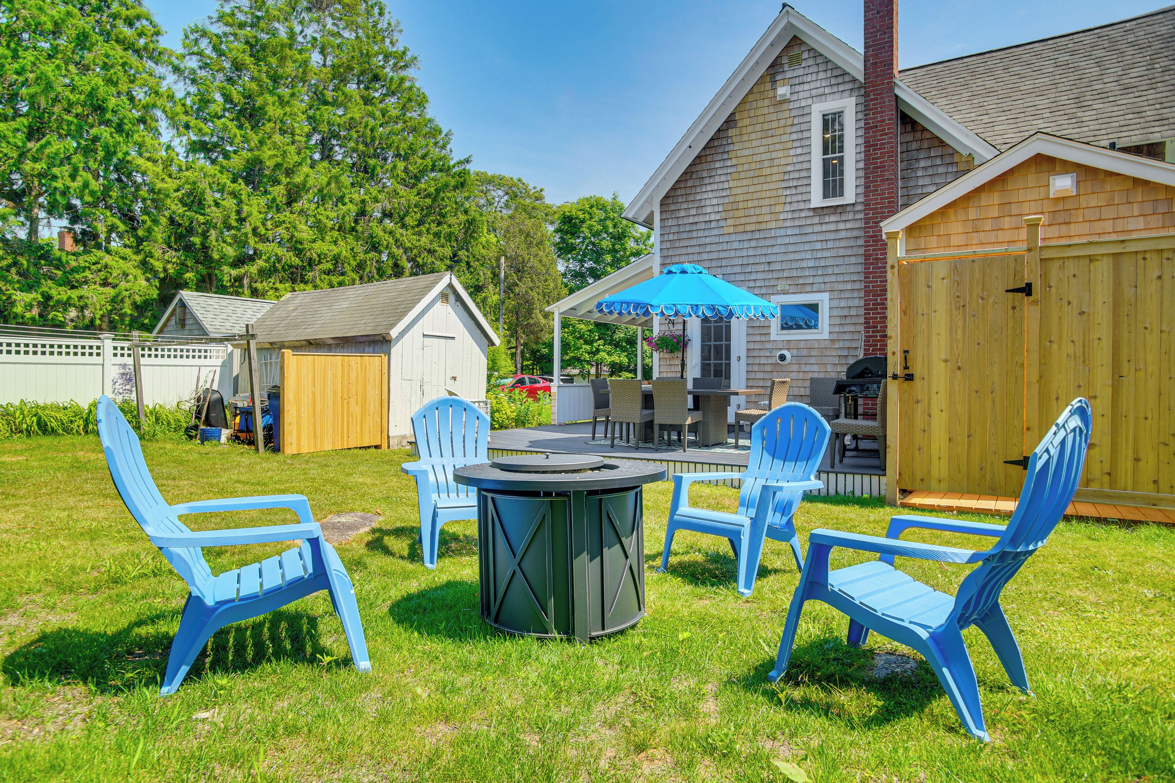A backyard with a round table, blue chairs, and a barbecue grill.