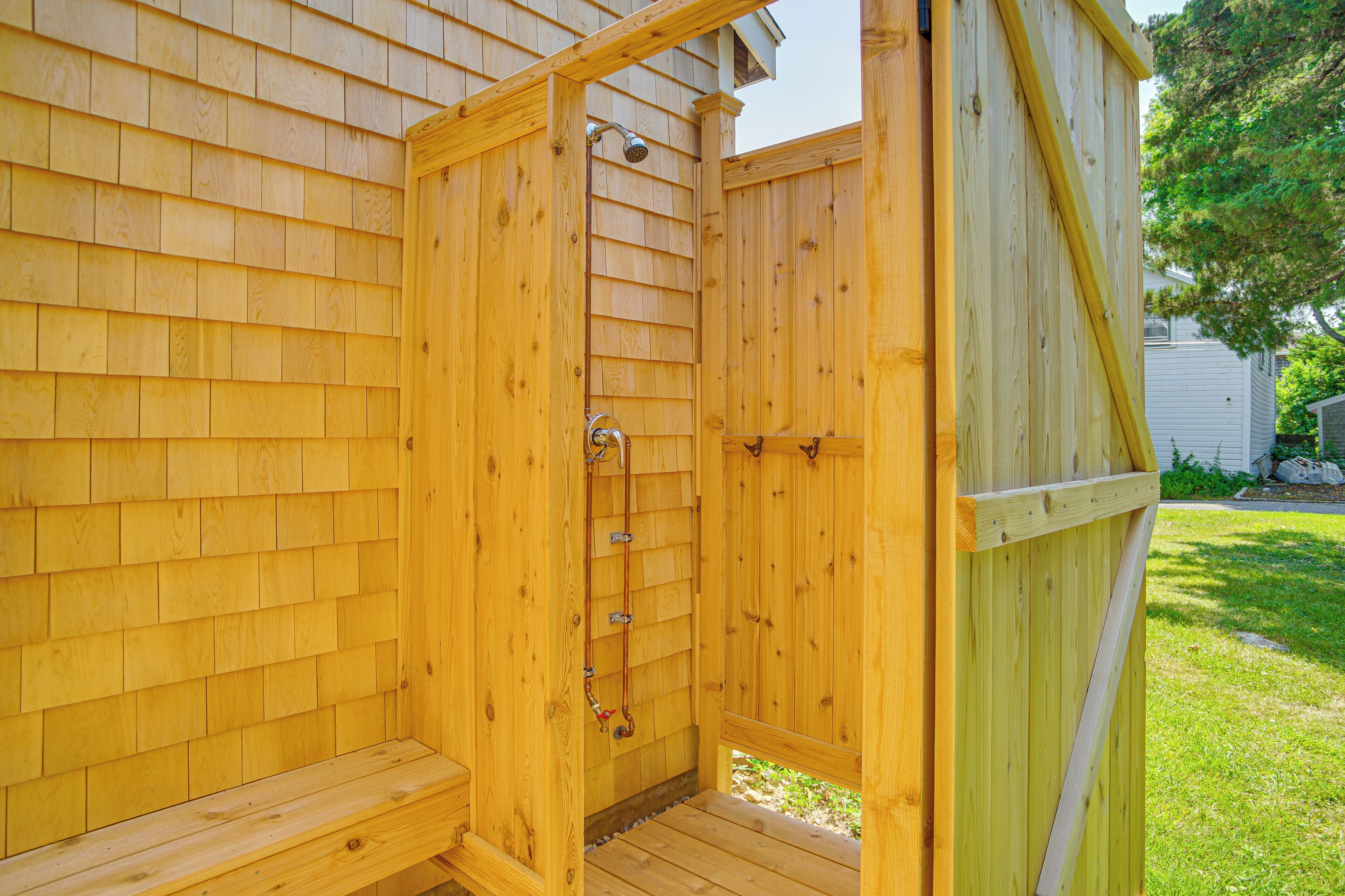 A wooden outdoor shower enclosure with a bench, a showerhead, and a hose.