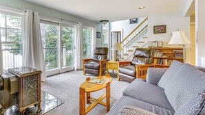 A spacious living room with a large window, a fireplace, a sofa, and a bookshelf. - Lakefront New London Retreat w/ Dock & Hot Tub! (New London)