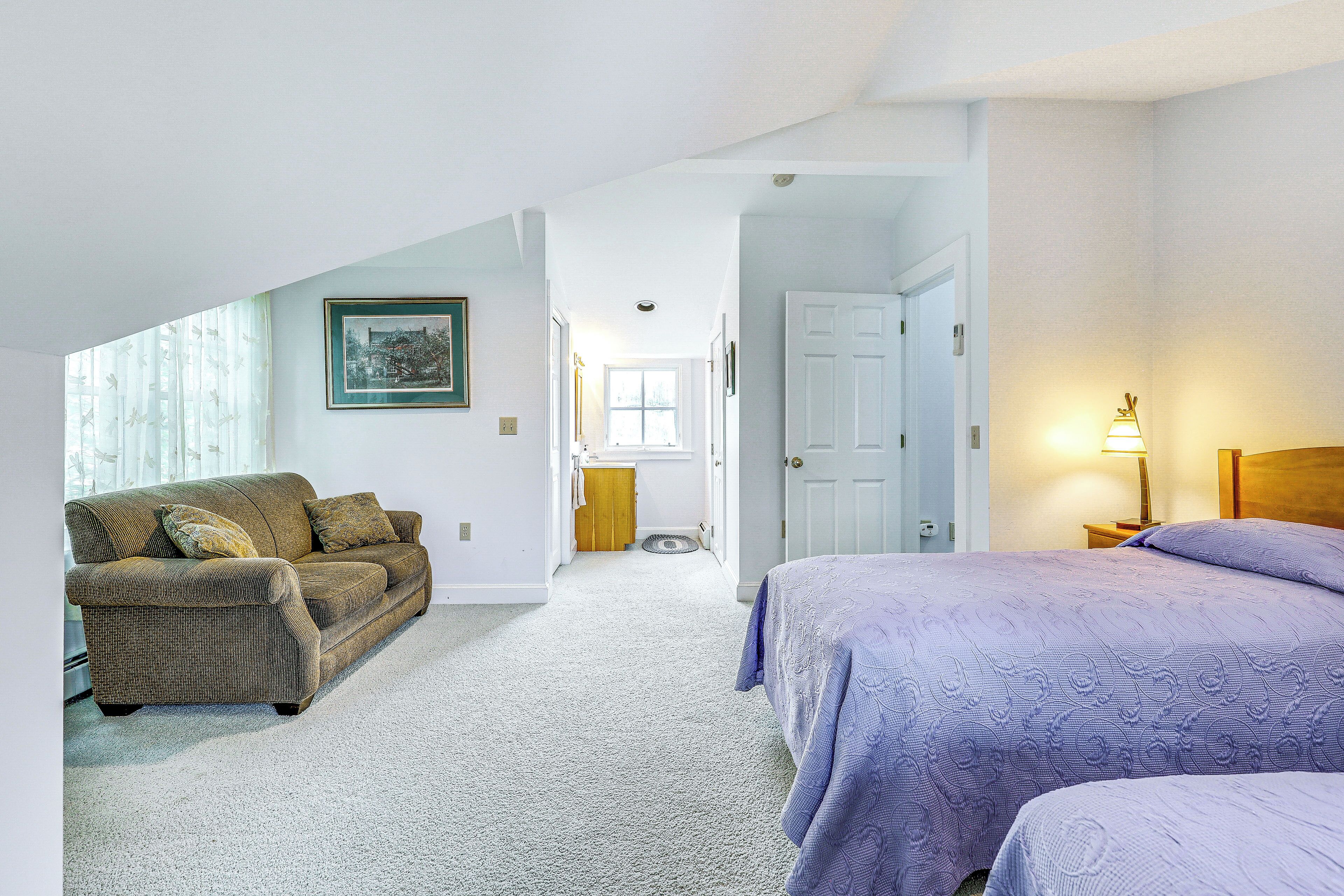 A bedroom with a bed, a couch, and a door leading to another room.