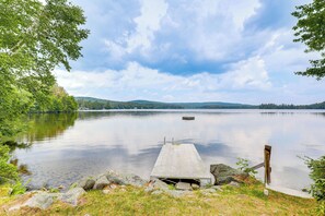 A calm lake with a wooden dock extending into the water, surrounded by greenery and hills in the background.