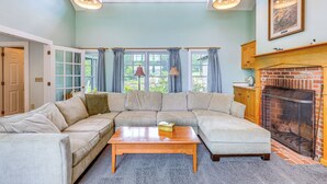 A living room with a sectional sofa, a fireplace, and large windows. - Lakefront New London Retreat w/ Dock & Hot Tub! (New London)