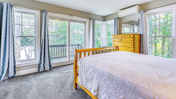 Une chambre dotée d’un grand lit, d’une commode en bois et de plusieurs fenêtres donnant sur l’extérieur.