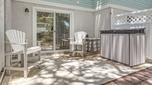 Un patio cubierto con dos sillas Adirondack, una parrilla y una puerta corrediza de vidrio que da a un jardín trasero.