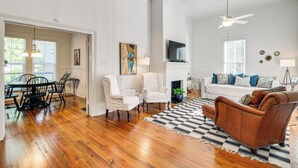 A spacious living room with hardwood floors, a fireplace, a television, and a ceiling fan. - Charming Georgia Cottage ~ 19 Mi to Statesboro! (Metter)