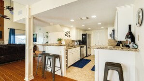 A modern kitchen with white cabinets, a granite countertop, and a blue rug. There are two bar stools and a ceiling fan.