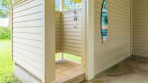A covered outdoor area with a shower and a surfboard on the wall.