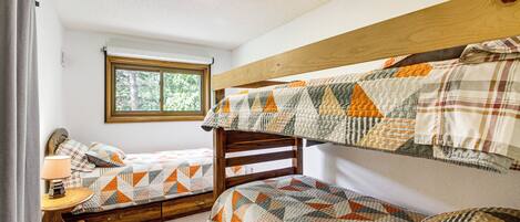 A room with bunk beds, a window, a lamp, and a wooden headboard.