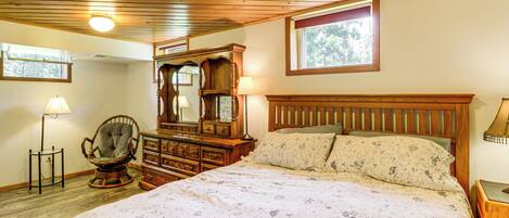 Ein Schlafzimmer mit einem großen Bett, einem Holz-Kopfteil, einem Schaukelstuhl, einer Kommode und einem Fenster, das für natürliches Licht sorgt.