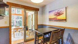 Ein Essbereich mit Tisch und Stühlen, einem Gemälde an der Wand und Blick durch eine Glastür in einen Außenbereich mit Tisch und Stühlen.