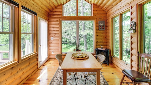 Ein Blockhaus-Interieur mit einem Holztisch, Stühlen und großen Fenstern mit Blick auf den Wald.