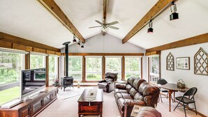 Ein geräumiges Wohnzimmer mit großem Fernseher, Ledersofas, einem Kamin und großen Fenstern mit Blick ins Freie.