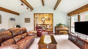 Ein Wohnzimmer mit einer Ledersofa, einem Holztisch und einem Flachbildfernseher.