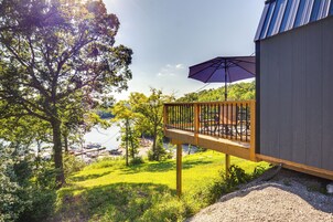 Una terraza de madera con barandilla que da a un lago, rodeada de follaje.