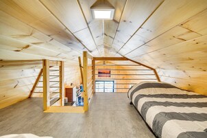 Un dormitorio en ático con techos altos, una escalera de listones de madera, una cama con colcha a rayas y un tragaluz.
