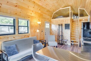 Un interior de cabaña acogedor con sofá, sillones, una mesa, chimenea y zona de entrepiso.