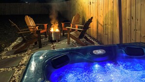 Un bain à remous doté d’un panneau de commande numérique, deux fauteuils Adirondack, un petit foyer et des guirlandes lumineuses.