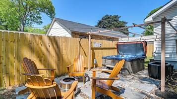 Un patio trasero con una terraza de madera, sillas Adirondack, una parrilla y un jacuzzi.