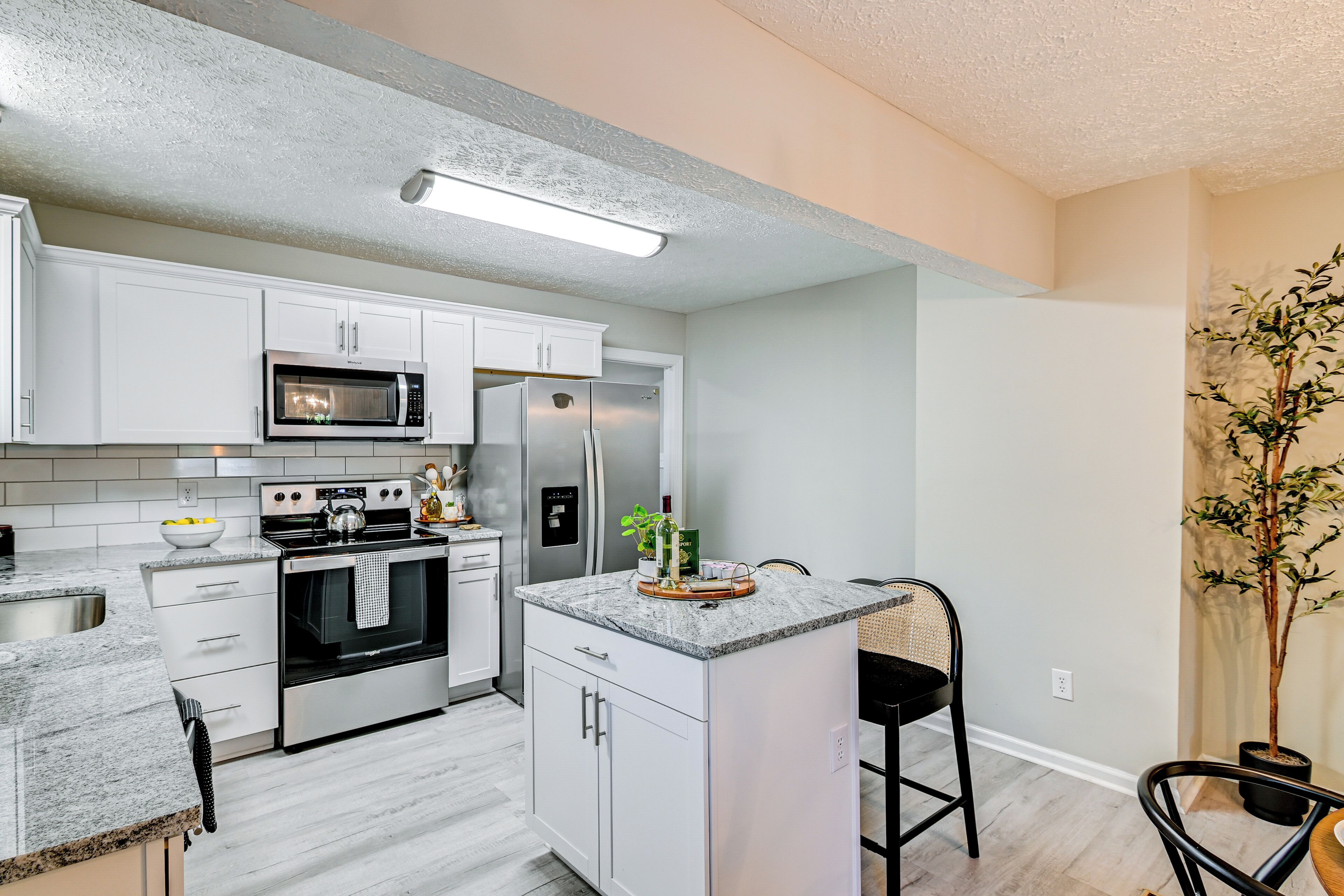 A modern kitchen with white cabinets, stainless steel appliances, a granite countertop, and a small island with bar stools.