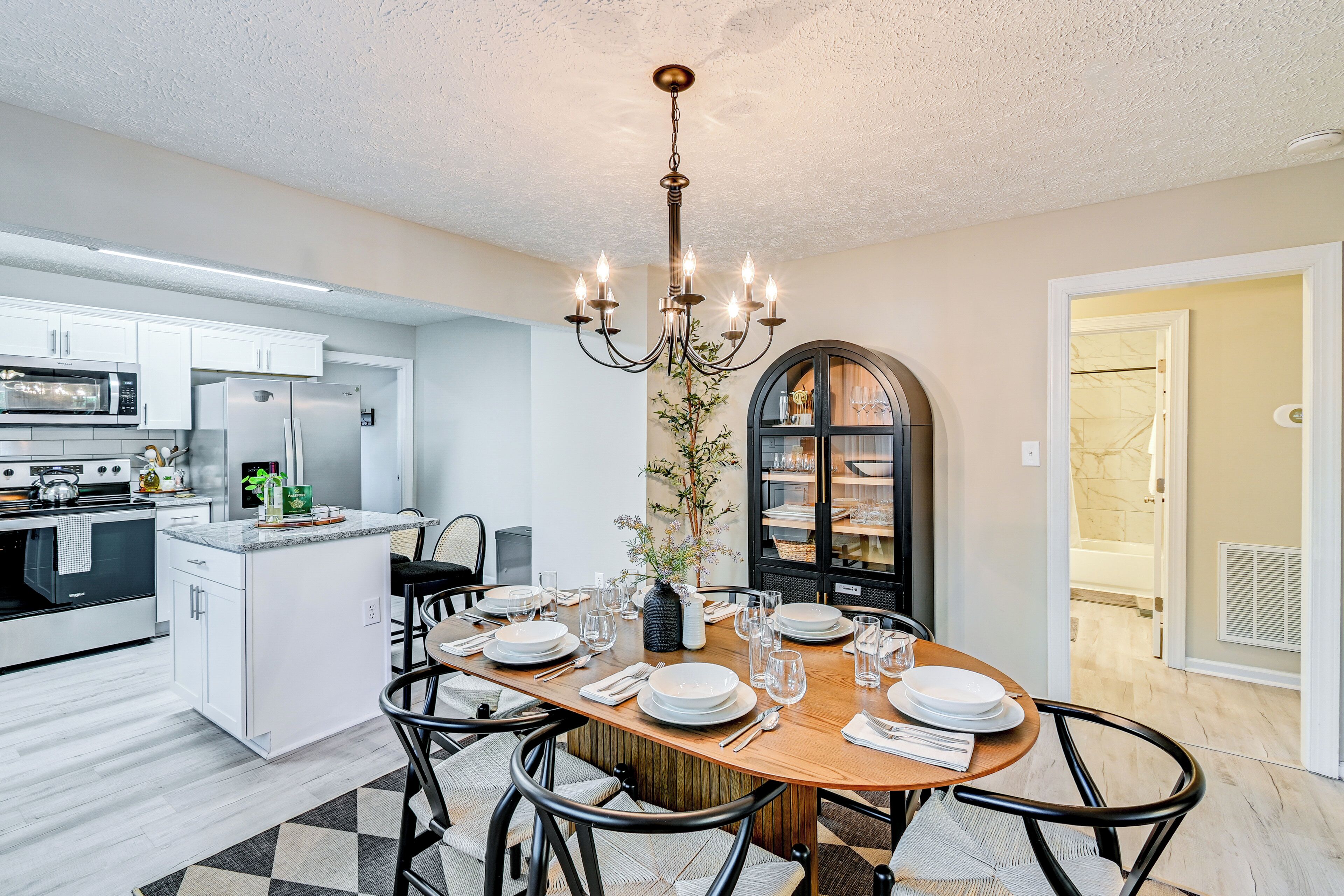 A modern kitchen with white cabinets, a central island, and a dining area with a wooden table set for six.