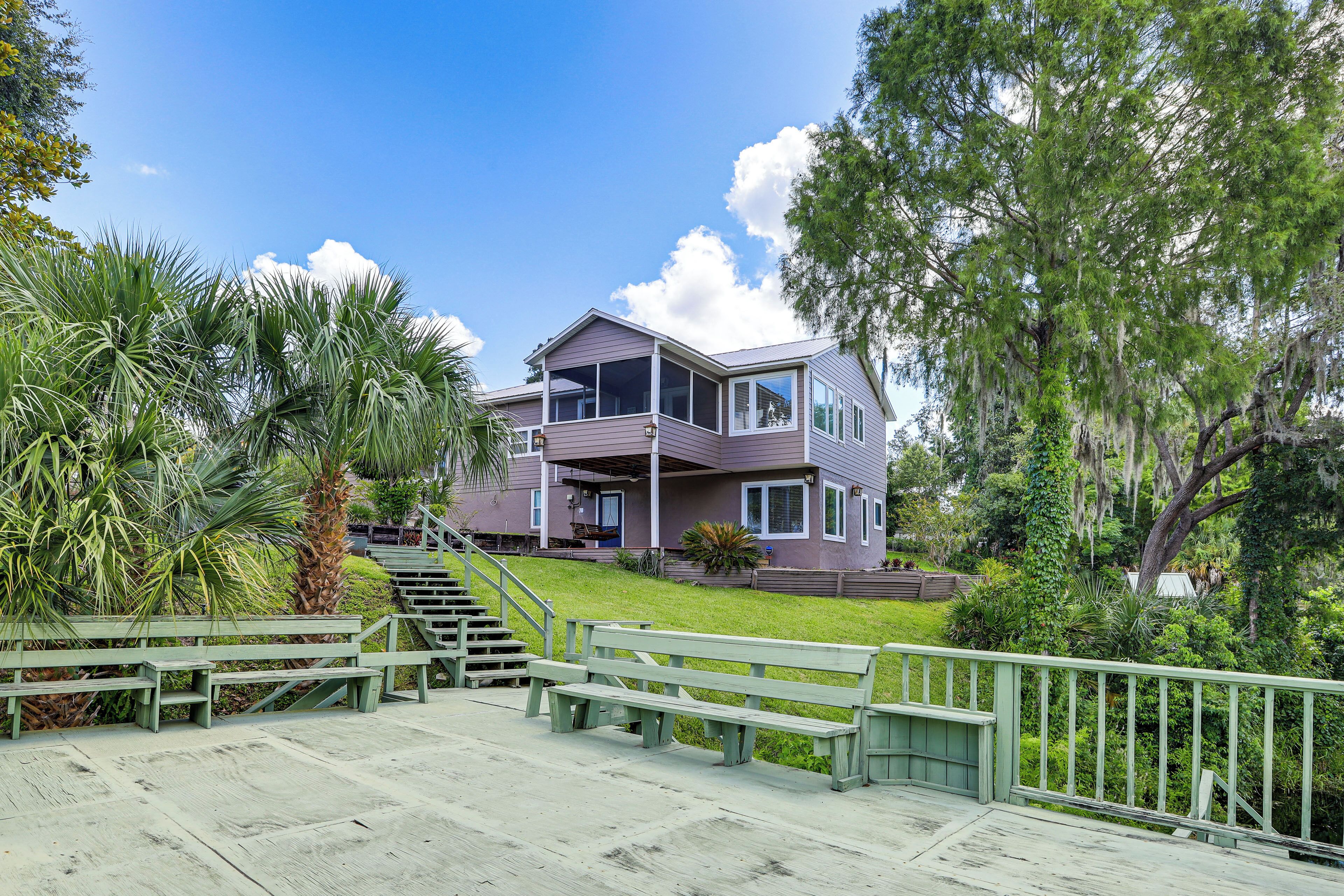 A modern two-story house with a balcony, surrounded by lush greenery and a wooden deck with benches.