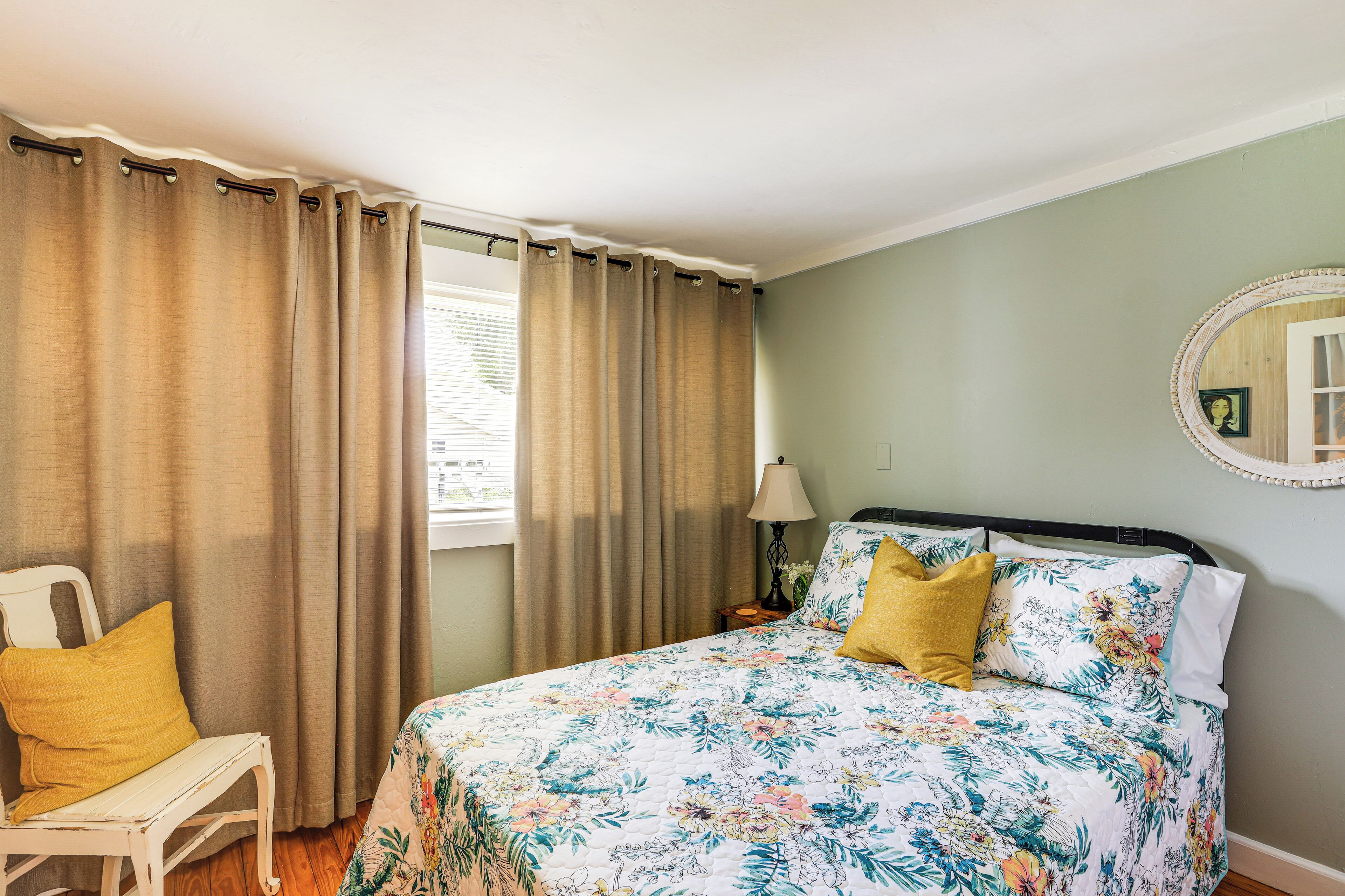 A bedroom with a floral bedspread, a bedside lamp, and a chair with a yellow pillow.
