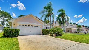 A suburban house with a garage, well-maintained lawn, and palm trees.