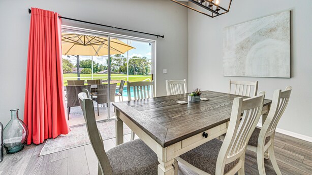 A dining area with a wooden table and chairs, a red curtain, and a view of a pool through large glass doors.