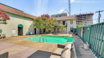 Uma área de piscina com espreguiçadeiras, uma piscina pequena e um edifício com toldo verde.