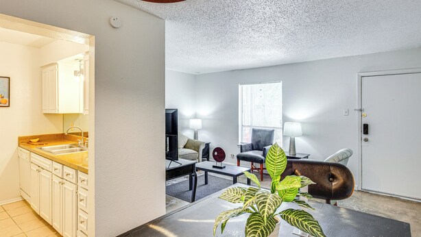 A modern living room with a sofa, armchair, and coffee table. There is a kitchen area with a sink and cabinets. A large window provides natural light. - Dallas Condo in Walkable Knox Street District! (Dallas)