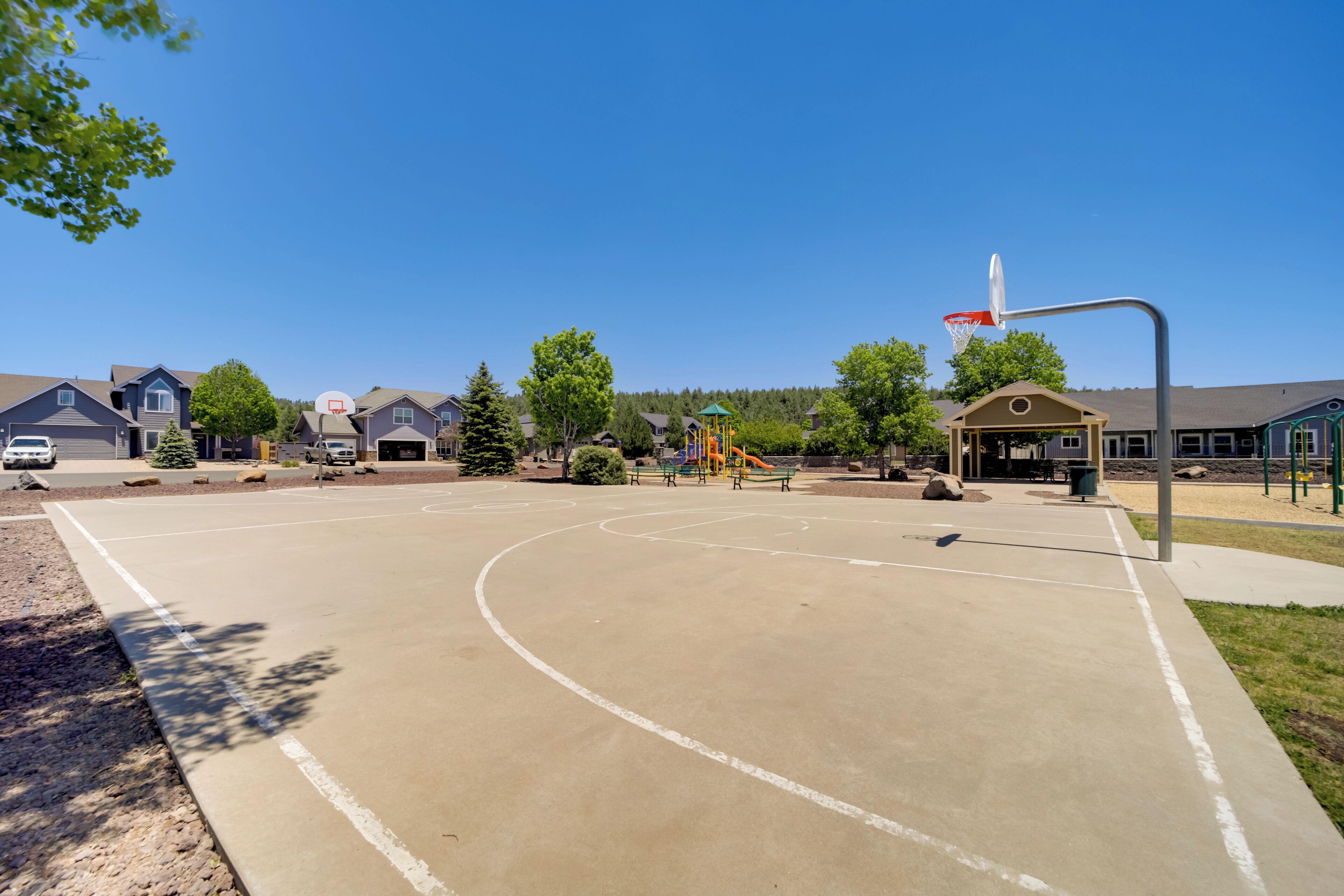 Una cancha de baloncesto con aro, bancos y juegos infantiles.