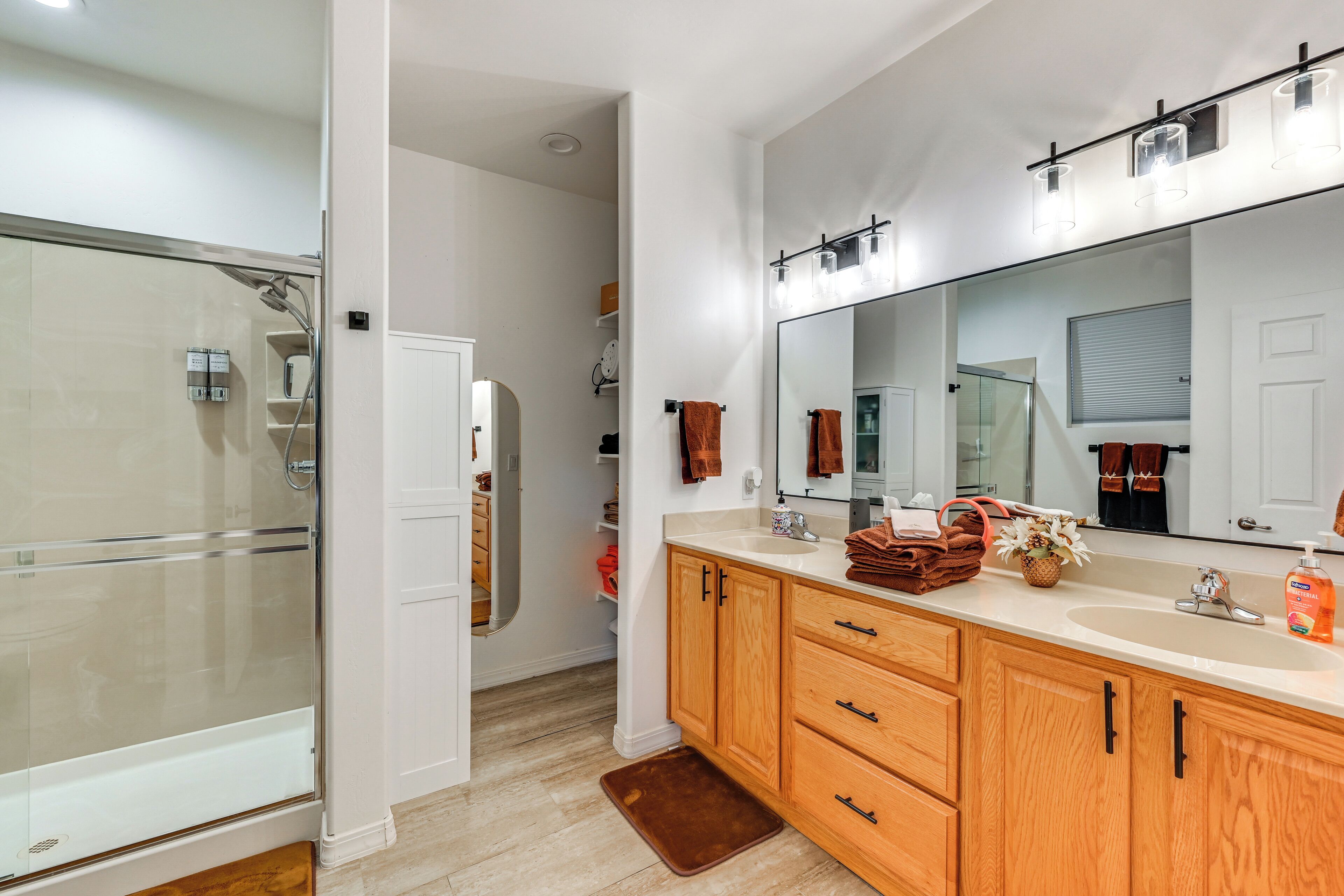 A modern bathroom with a glass shower enclosure, wooden vanity with a sink, and a large mirror.
