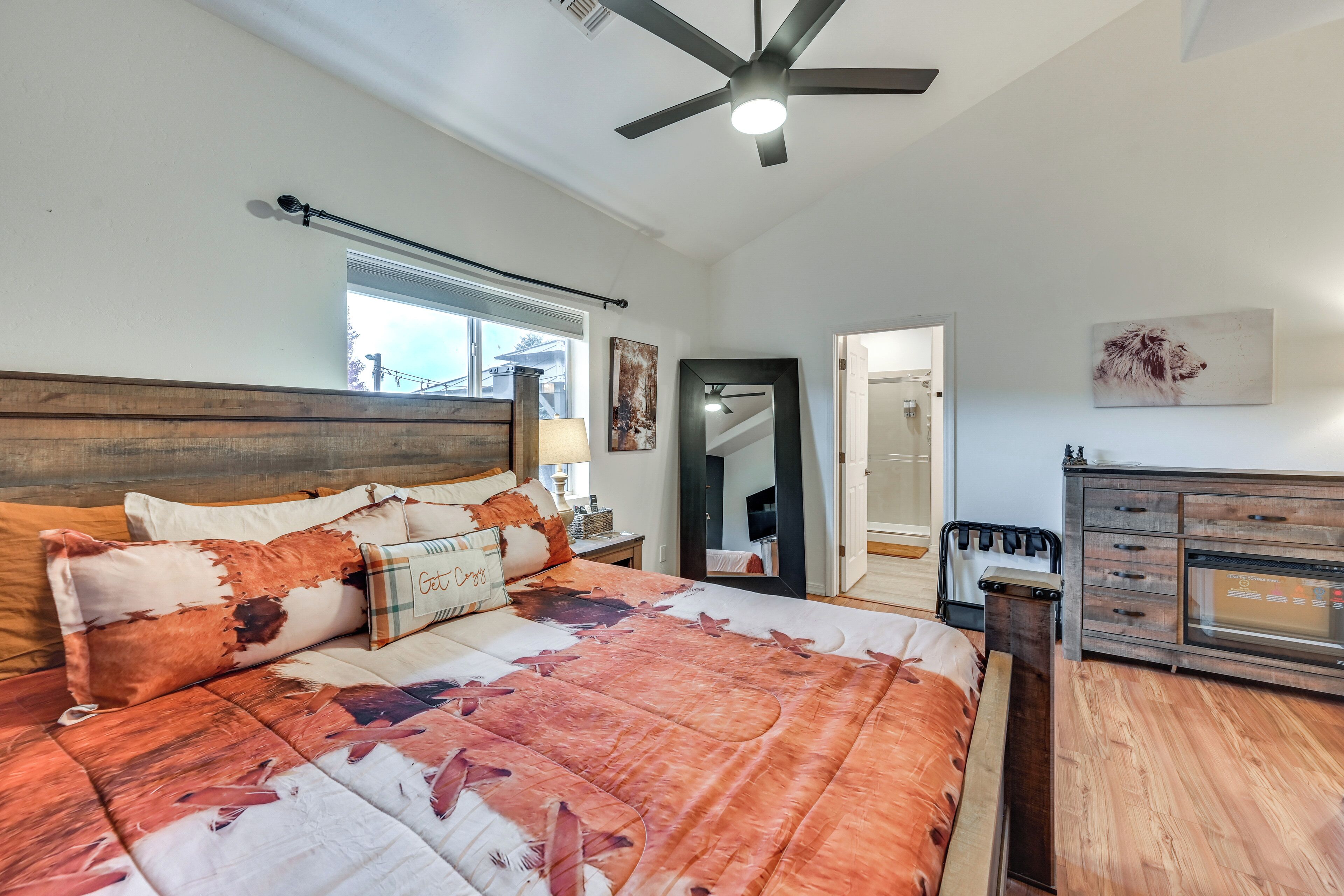 Une chambre avec un grand lit, un ventilateur de plafond, une commode en bois et une fenêtre avec des stores.
